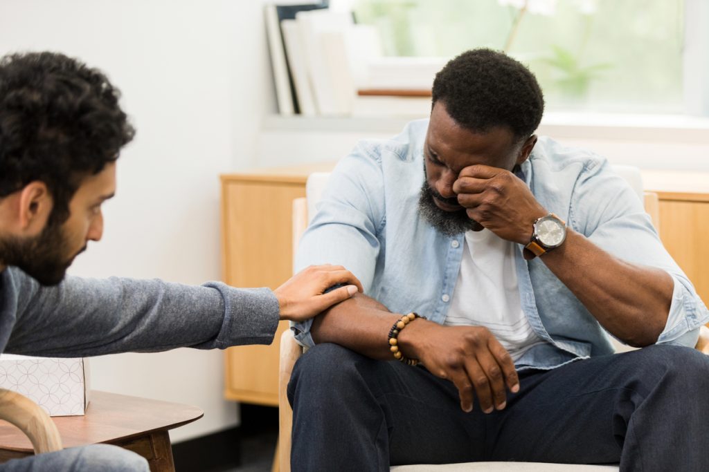 young male counselor reaches out to comfort distressed male client